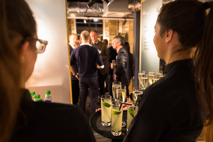 Waiters hold trayed drinks whilst guests enter reception area 