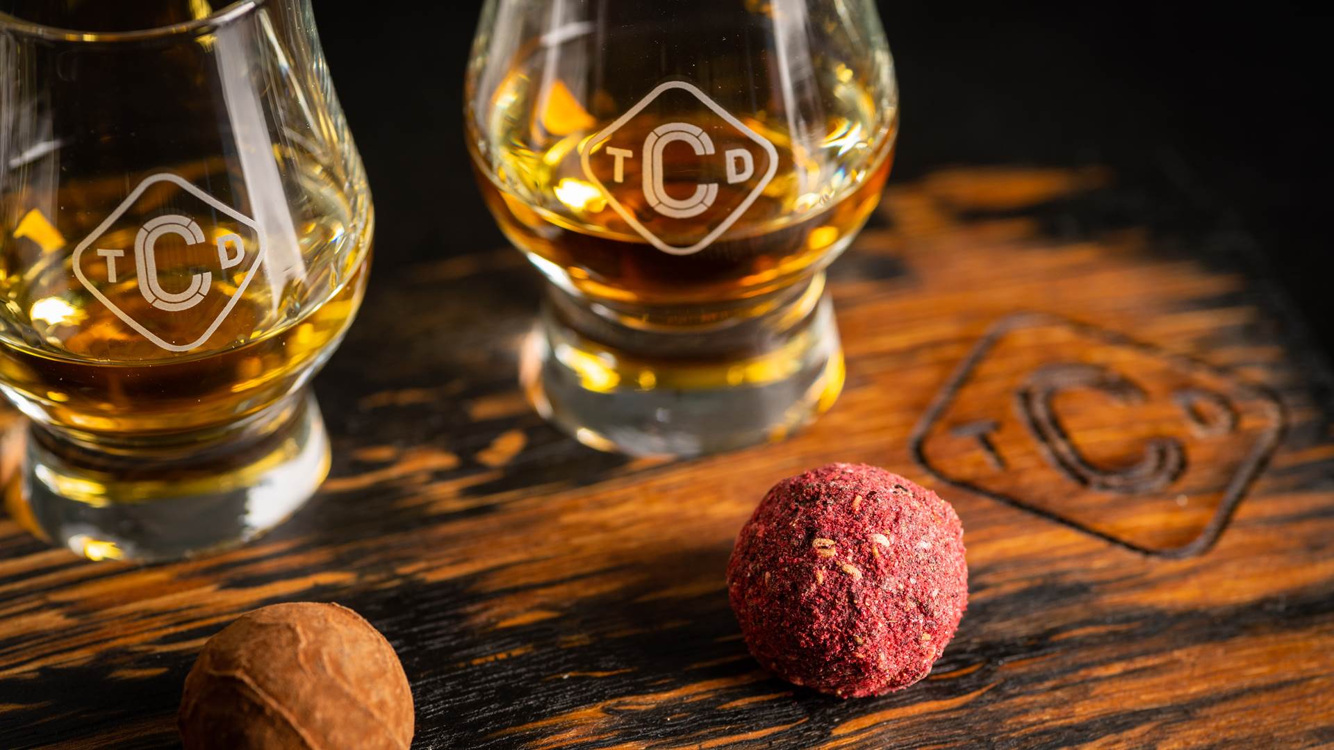 Close up of whisky & chocolate pairing, includes dram of whisky and round coated pink truffle chocolate